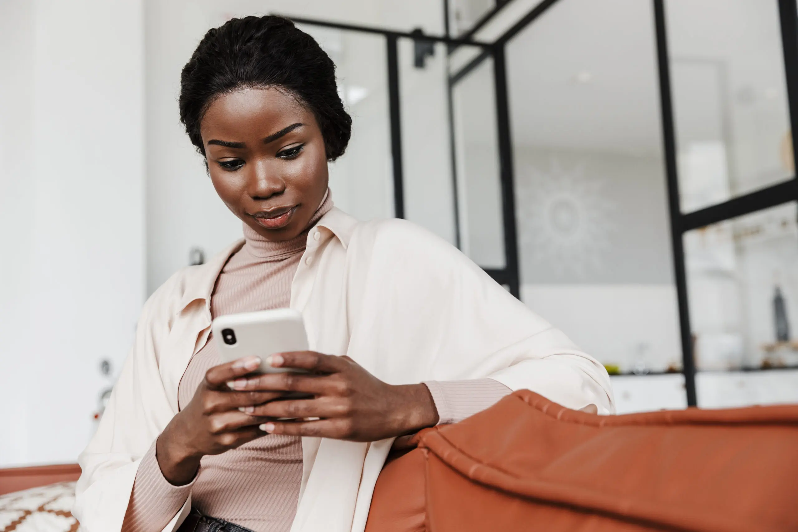 Image of serious young african woman sitting on sofa indoors at